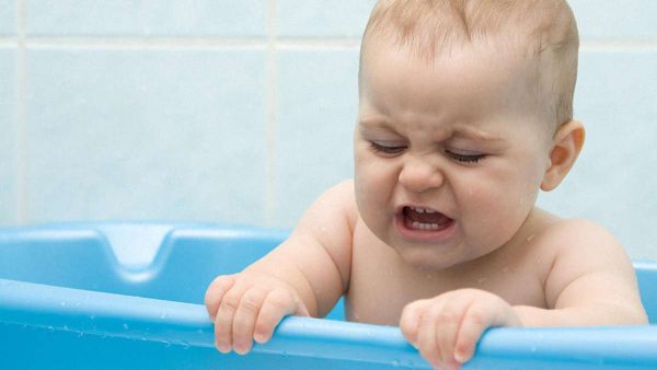 Ребенок сидит в голубой ванночке и плчет