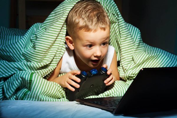 Мальчик играет в компьютерные игры под одеялом